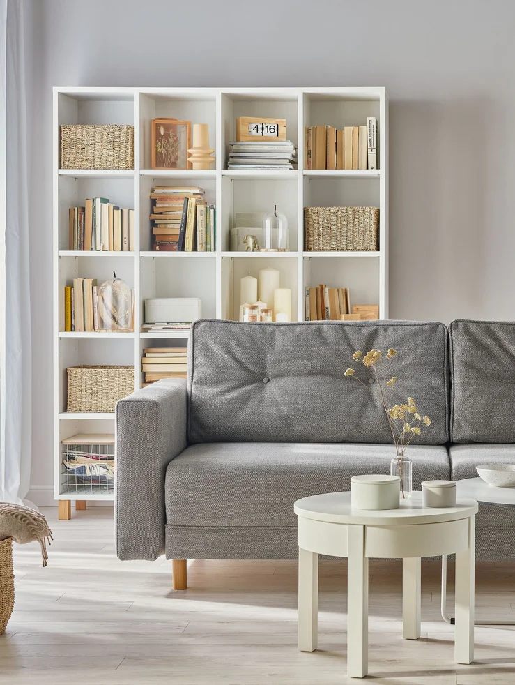 Minimalistyczny salon z szarą sofą i białym regałem.